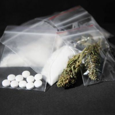 A photo of an array of leaf, powder and pill drugs in plastic bags on a black background.